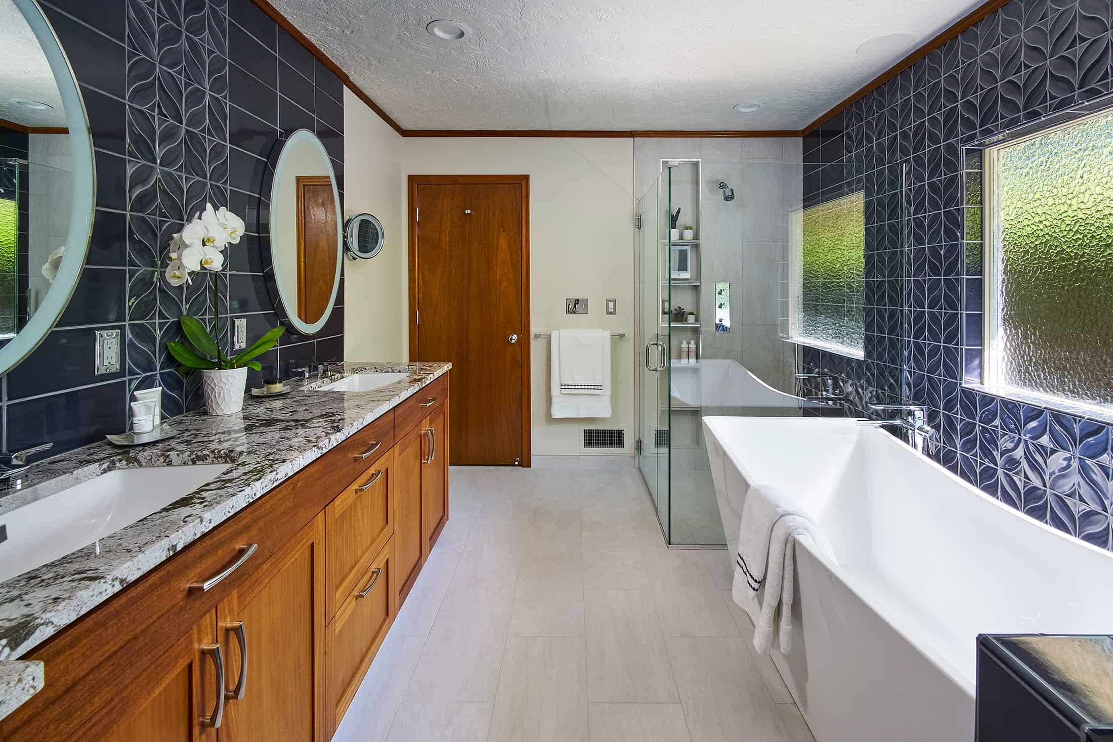 Spacious bathroom with freestanding tub and glass shower featuring blue custom tile work